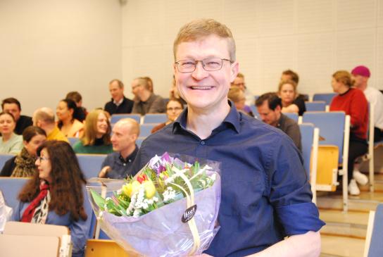 Morten Munthe er årets Holmboeprisvinner. Mann med blå skjorte og blomster står foran et auditorium. Han smiler. 