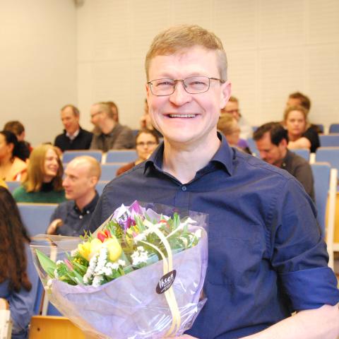 Morten Munthe er årets Holmboeprisvinner. Mann med blå skjorte og blomster står foran et auditorium. Han smiler. 